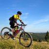 Cyclist man riding electric mountain bike outdoors. Male tourist biking along grassy trail in the mountains, wearing helmet and backpack. Concept of sport, active leisure and nature.