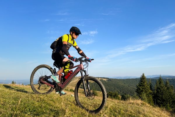 Cyclist man riding electric mountain bike outdoors. Male tourist biking along grassy trail in the mountains, wearing helmet and backpack. Concept of sport, active leisure and nature.